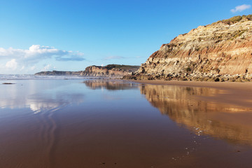Fototapeta na wymiar Mountain reflected in the smooth water of the beach Areia Branca. Lourinha, West coast of Portugal