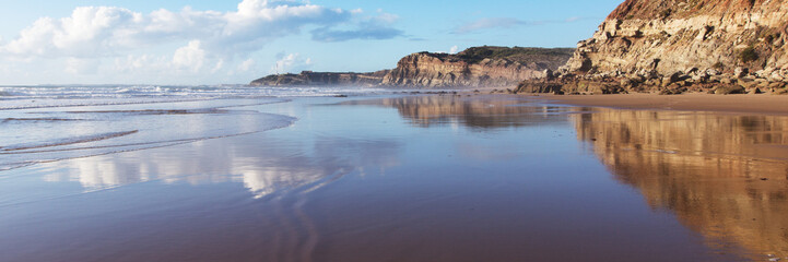 Mountain reflected in the smooth water of the beach Areia Branca. Lourinha, West coast of Portugal
