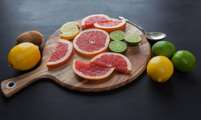 Citrus fruits arrangement with vintage silver spoon on black painted surface with back lighting.