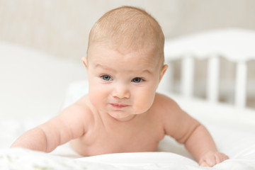 Cute baby gets on arms in crawling position in bed after nap time, raises with effort head and chest