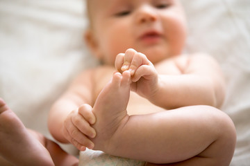 Adorable baby taking an interest in his feet, amusing himself, playtime. Closeup. Family, baby development photo. Focus on a leg © fizkes