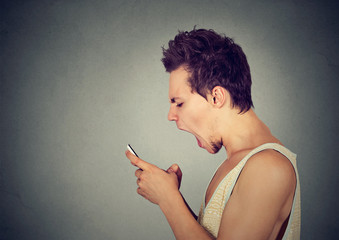 Side profile portrait angry young man screaming on mobile phone