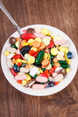 Medical pills on teaspoon and heap of colorful medical capsules in background, health care concept