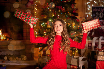 Girl at Christmas with a Christmas tree, fireplace and gifts at home, decorates the Christmas tree, gifts received