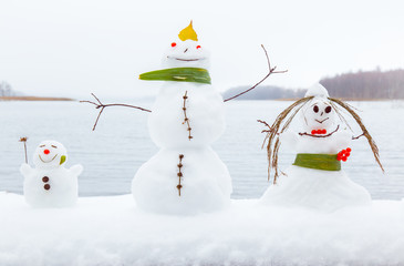 Portrait of very nice, smiling family of snowmens in winter on the lake background. Positive mood.