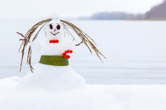 Portrait of very nice, smiling snowman - snow girl with long hair and skirt in winter on the lake background. Positive mood.