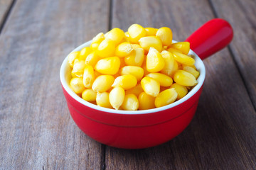 Close up of cooked sweet corn seeds in a red bowl on a wooden table.
