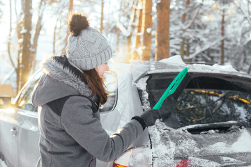 Fototapeta na wymiar Happy girl cleaning her car of snow in a forest