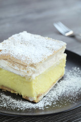 Cream Cake with sugar icing on a black plate and wooden table