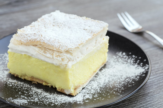 Cream Cake with sugar icing on a black plate and wooden table