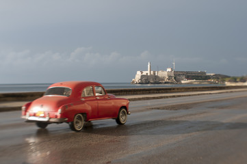 Dreamy tilt-shift scenic view of vintage American car taxi driving in front of el Morro lighthouse along the Malecon in Central Havana, Cuba