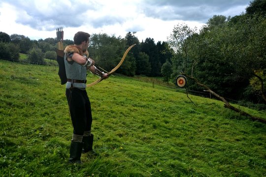 Junger Mittelalterliche Bogensch&uuml;tze von der Seite  , zielt mit Pfeil und Bogen auf Strohscheibe in gr&uuml;ner Natur