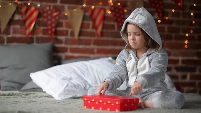 Cute little girl is unhappy with her Christmas gift by a fireplace in a her bed on Xmas morning
