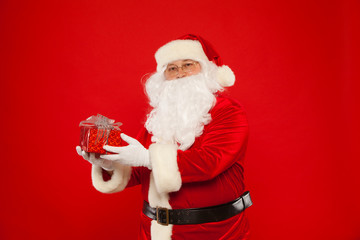Photo of Santa Claus gloved hand with giftbox, on a red background. Christmas