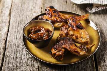 Grilled chicken wings with chutney on a plate with the effect of craquelure on rough wooden background. Selective focus