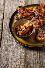 Grilled chicken wings with chutney on a plate with the effect of craquelure on rough wooden background. Selective focus. Toned image 