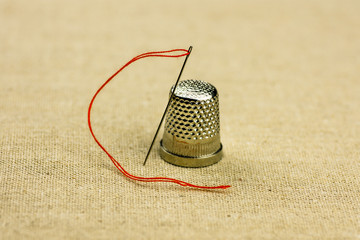 Thimble and sewing needle with a thread on linen fabric, warm tone