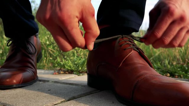 man ties up leather shoes in the park - detail 