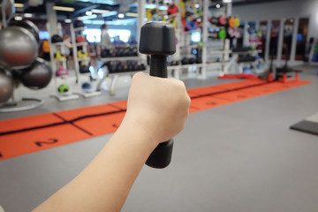 Hands holding dumbbells in sport club or gym and fitness room.