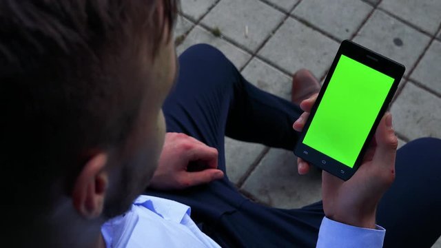 young man sits on the bench and works on smartphone - green screen 