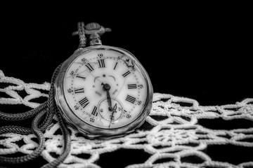 Artistic low key image of antique broken pocket watch on black velvet fabric and white lace. Monochromatic processing. 