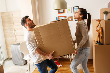 Young married couple carrying big cardboard box into new home. Moving house.	 - obrazy, fototapety, plakaty