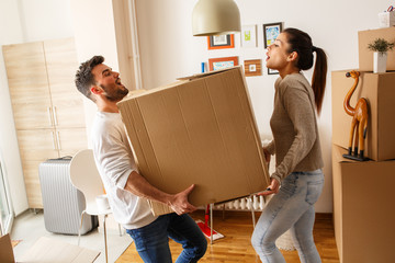 Young married couple carrying big cardboard box into new home. Moving house.	