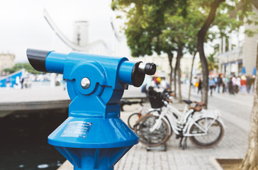 Touristic telescope look at city with view of Barcelona Spain, closeup blue binoculars on background viewpoint the port yacht and cycle bike, coin operated  in panorama observation nature