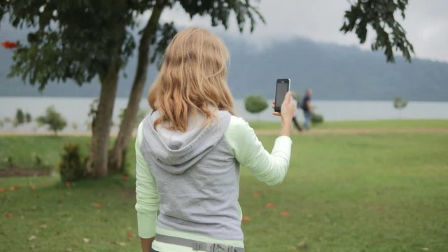 Young woman looking at map and playing an augmented reality mobile game on a phone walking around in the park. Using location based app with camera to interact on smartphone