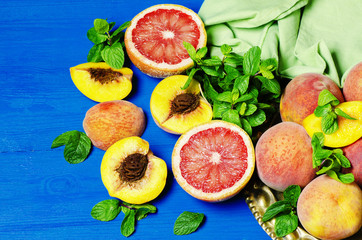 Fresh fruits -Slices of  grapefruits and peaches with fresh mint on blue wooden table. Top view with copyspace