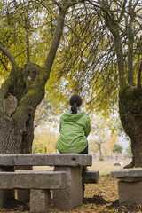 Fototapeta premium Woman sitting on a park bench with yellow leaves falling from trees
