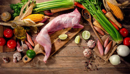 Raw rabbit with vegetables and fresh herbs on rustic background.