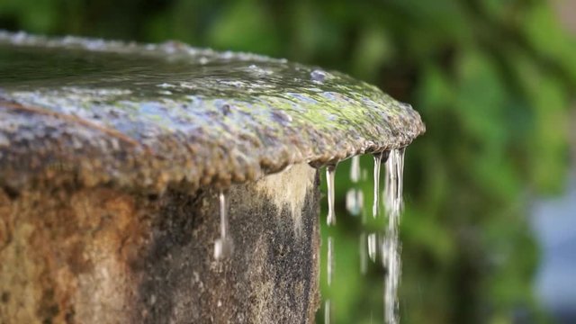 detail of water overflows from a stone fountain and falls slowly, slow motion with green background