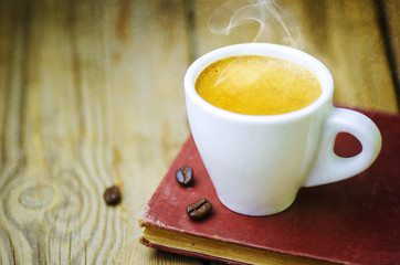 Cup of Coffee Espresso placed with an old book and  roasted coffee beans on a rustic wooden table. 
