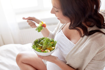 close up of pregnant woman eating salad at home