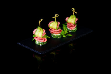 canape salami cucumber on black background with reflection