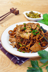 yi mein noodle stir fried with dark caramel sauce on wooden table, served together with a small plate of sour taste green chili, makes a delectable authentic malaysian chinese street food.