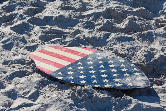 Small surfboard with american flag pattern on the beach.