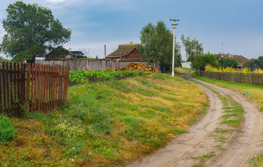 Fototapeta na wymiar Autumnal scenery with earth road between streets in Boromlya village, Sumskaya oblast, Ukraine