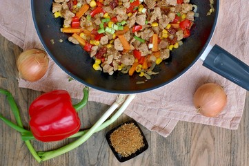 Ragout from pork meat, red pepper, onion, spring onion, carrot and spices in black pan on grey cloth on dark wooden background