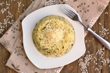 Creamy risotto with cucumber and cheese on white plate with fork on ..grown cloth on dark wooden background