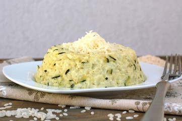 Creamy risotto with cucumber and cheese on white plate with fork on ..grown cloth on dark wooden background
