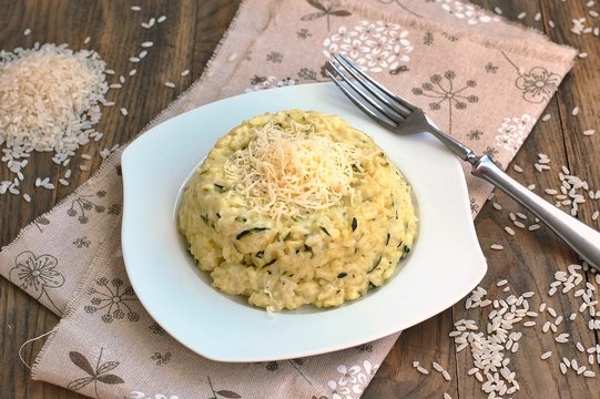 Creamy risotto with cucumber and cheese on white plate with fork on ..grown cloth on dark wooden background