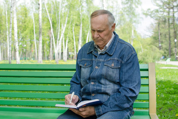 Fototapeta premium Aged man is making notes in the daily planner in the park