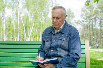 Aged man is making notes in the daily planner in the park