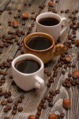 Three cups of coffee, hazelnuts and cocoa beans on wooden background