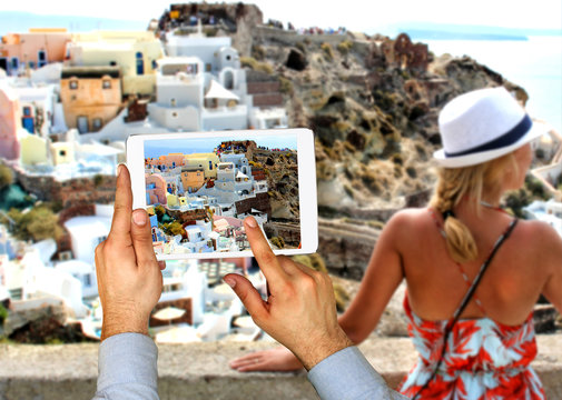 Tourist man taking picture with touch pad in Oia town on Santorini island. Travel concept.  Europe summer travel destination in Greece, Caldera, Aegean sea.;