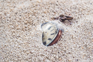 Sands of time, antique rotten pocket watch partial buried in the sand