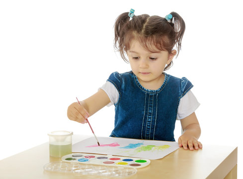 Little girl paints with watercolors at the table.