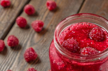 Close-up raspberry jam in glass jar. Fresh raspberry on wood table